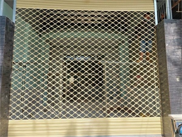Cửa cuốn mắc võng sơn tĩnh điện màu vàng kem đóng ở mặt tiền nhà, hai bên là trụ ốp gạch tối màu