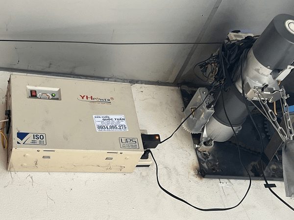 Bình lưu điện cửa cuốn YH Power đấu nối với motor, trên bình dán tem Cửa Cuốn Quốc Tuấn