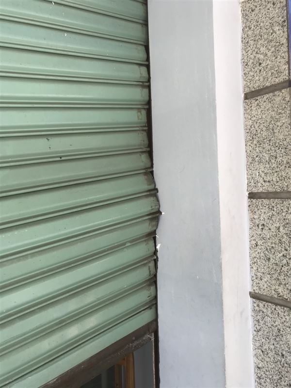 Cửa cuốn bị kẹt, lá cửa màu xanh phồng ra và lệch khỏi mép ray