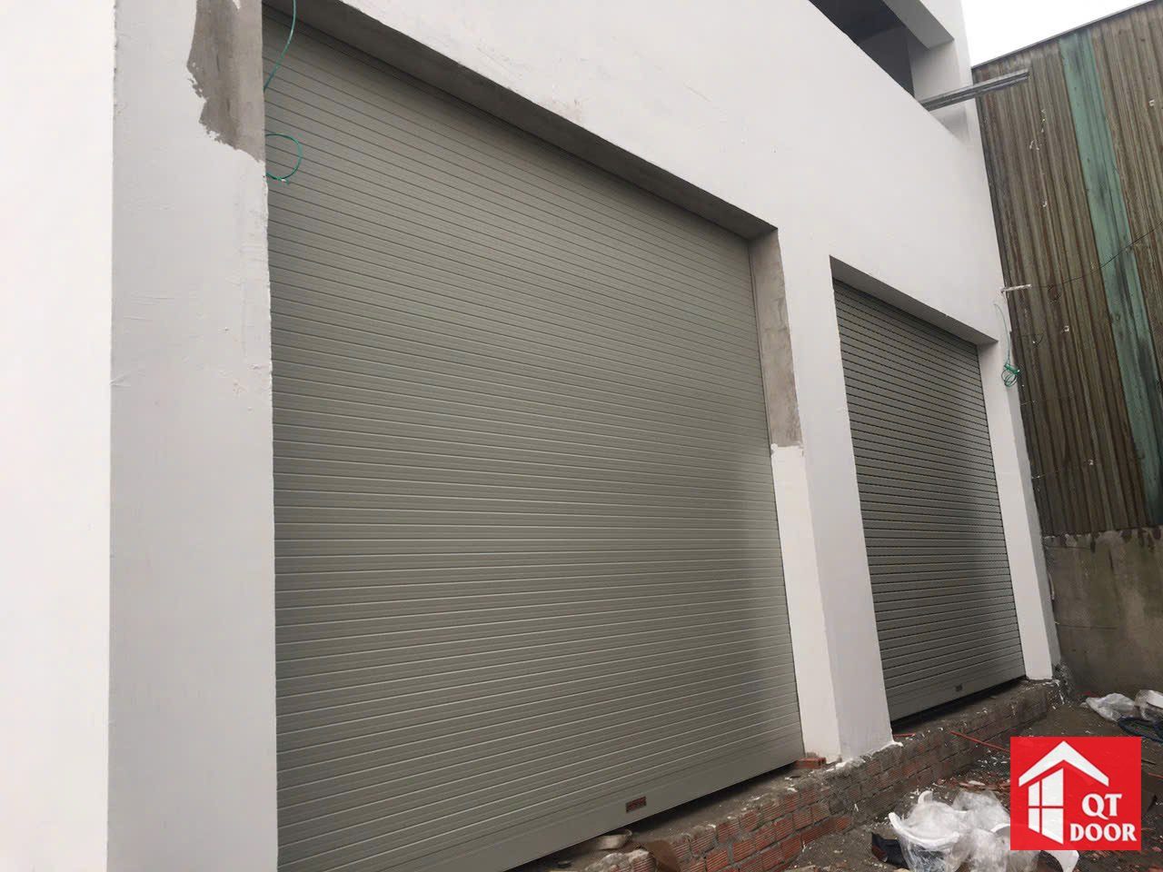 Hai cửa cuốn màu ghi xám lắp cạnh nhau ở ô cửa tường mới xây