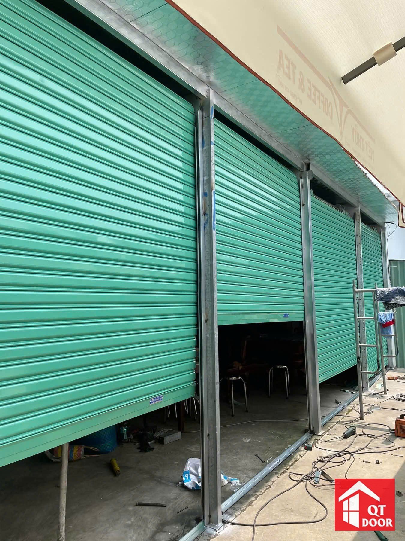 Dãy cửa cuốn lá tôn màu xanh ngọc đang lắp ở mặt tiền dãy cửa hàng
