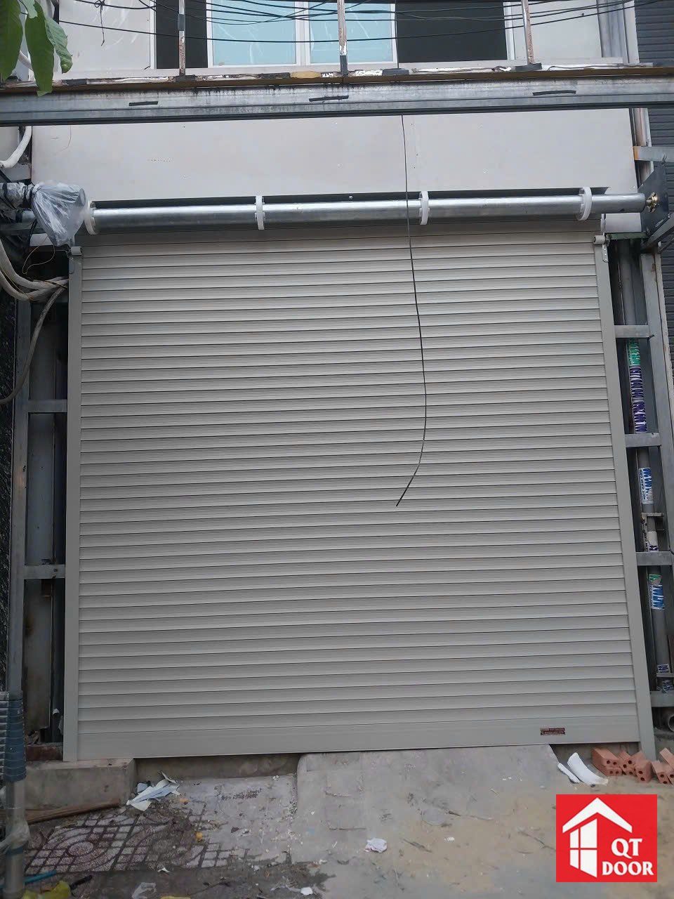 Cửa cuốn màu ghi vừa lắp ở mặt tiền nhà đang xây, ống trục và motor phía trên chưa có hộp che
