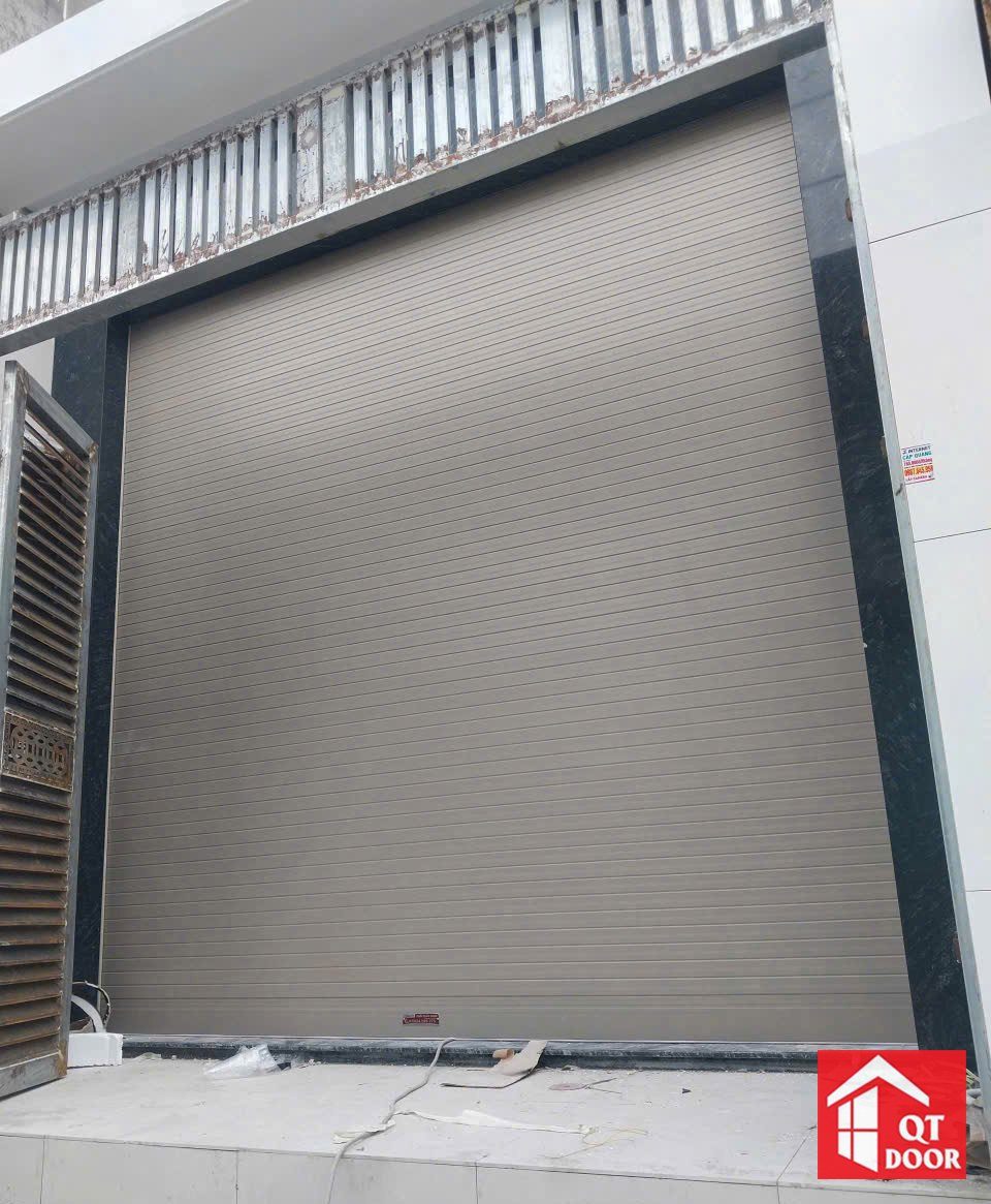 Cửa cuốn màu ghi lắp ở mặt tiền nhà phố mới xây, nền gạch trắng còn vật tư thi công