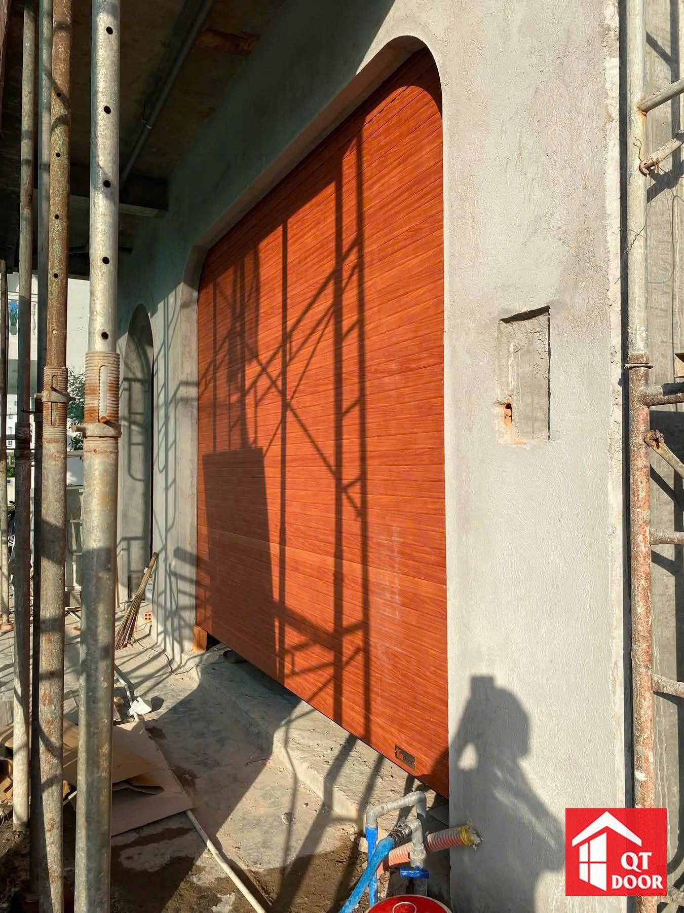 Cửa cuốn vân gỗ màu cam ở ô cửa vòm, giàn giáo còn dựng bên cạnh