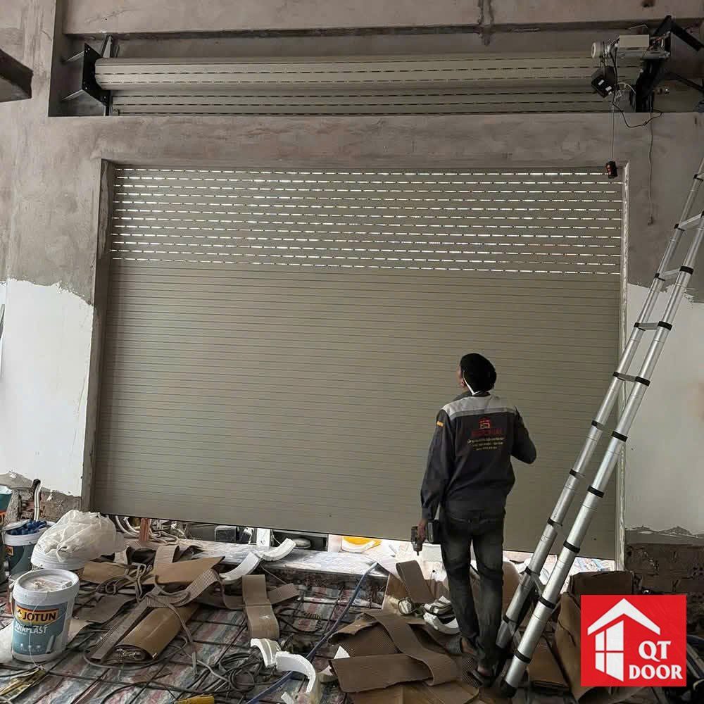 Thợ mặc đồng phục đứng kiểm tra cửa cuốn khe thoáng màu ghi vừa lắp, motor ở phía trên