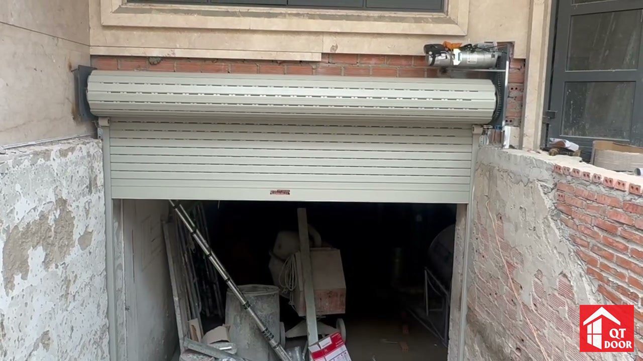 Cửa cuốn tự động lá có lỗ thoáng nhỏ đang kéo lên, ống trục và motor đặt phía trên ô cửa