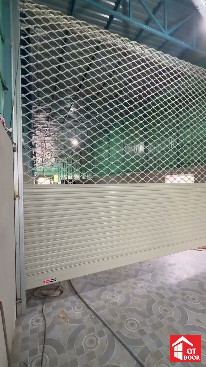 Cửa cuốn kết hợp phần lưới mắt cáo phía trên và lá kín phía dưới, lắp trong nhà xưởng mái tôn